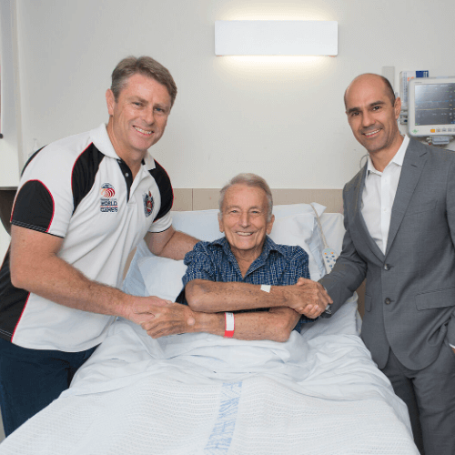 Two doctor holding hands with patient on bed